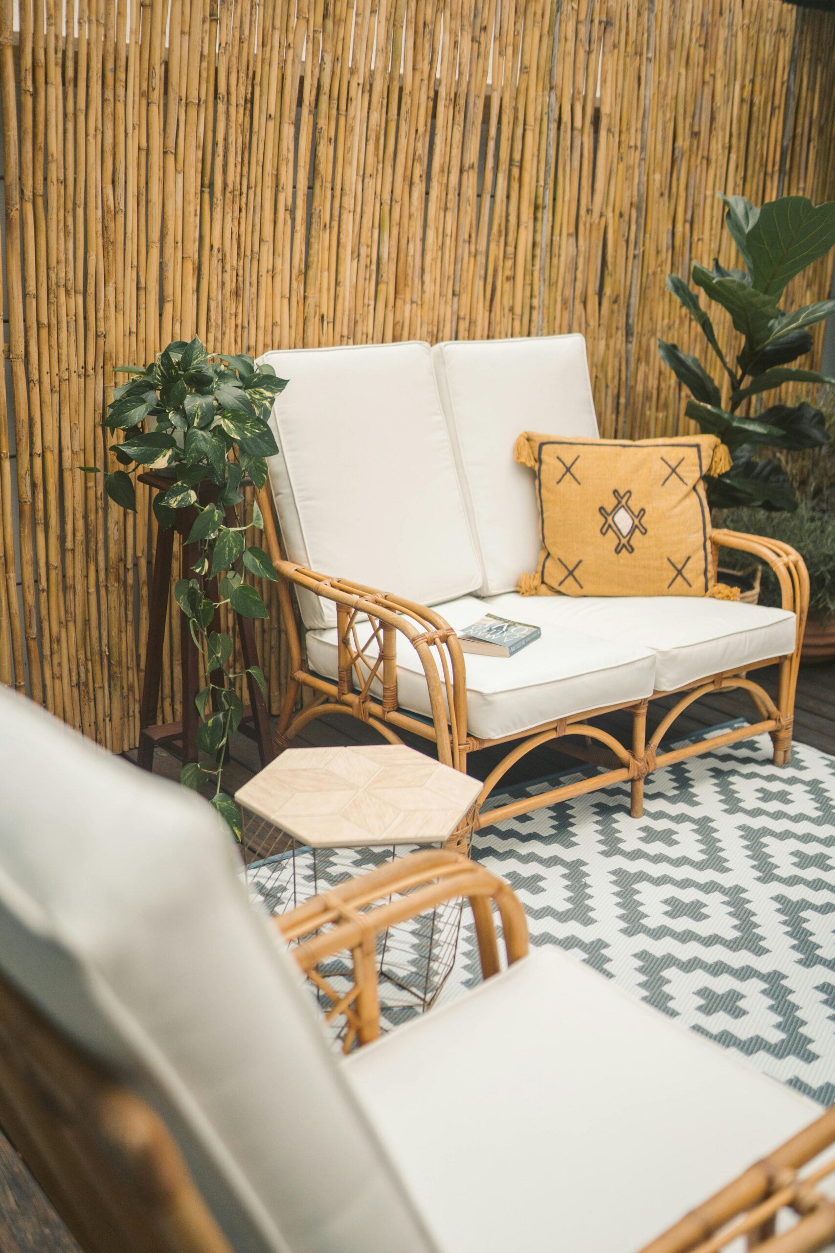 Inviting bamboo patio with a wooden sofa, throw pillow, and lush green plants for a cozy outdoor setting.